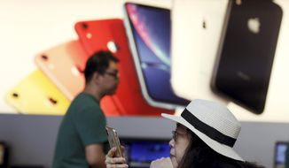 In this Friday, May 10, 2019, file photo, a customer looks at her iPhone at an Apple store in Beijing. (AP Photo/Ng Han Guan, File)