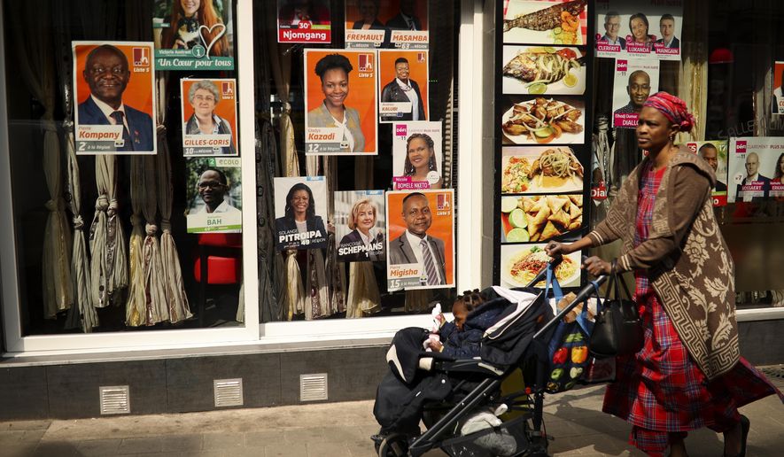 A woman walks past political campaign posters placed on a restaurant window at the African Matonge quarter in Brussels, Wednesday, May 22, 2019. Belgium, which has one of the oldest compulsory voting systems, will go to the polls for regional, federal and European elections on May 26, 2019. (AP Photo/Francisco Seco)