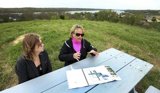 In a Tuesday May 7, 2019 photo Shive Hattery project manager Marti Ahlgren, left and property owner Marijo Anderson sit at a picnic table on top of a hill over looking the Mississippi River on the Anderson farm just south of Princeton, Iowa. The site could soon be certified as a green business park.  (John Schultz/Quad City Times via AP)