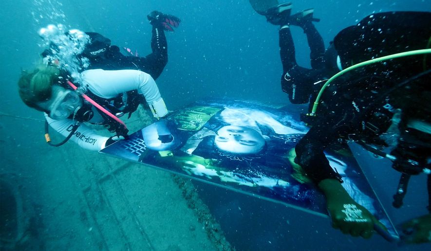 In this Friday, May 24, 2019, photo provided by the Florida Keys News Bureau, divers carry a large photo illustration to be hung on the superstructure of the 523-foot-long Gen. Hoyt S. Vandenberg that was intentionally sunk almost 10 years ago off Key West, Fla., in the Florida Keys National Marine Sanctuary. The artwork, one of 24 created by Austrian photographic artist Andreas Franke, is a part of his &amp;quot;Plastic Ocean Project&amp;quot; designed to communicate the need to protect the world&#x27;s oceans from plastic refuse. The entire series is to be on display on the former U.S. Air Force missile tracking ship for divers to view until Aug. 25, 2019. (Joe Berg/Florida Keys News Bureau via AP)