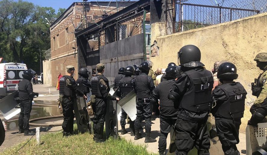 In this photo made available by Ukraine's Police Press Service, riot police stand at the prison in Odessa, Ukraine Monday, May 27, 2019. Police says four prison guards have been injured in clashes with inmates who have barricaded themselves in a prison in Ukraine's port city of Odessa. Serhiy Shaykhet, chief of the investigative unit at the Odessa police, said in televised remarks Monday that police are negotiating with the inmates. (Ukrainian Police Press Office via AP)