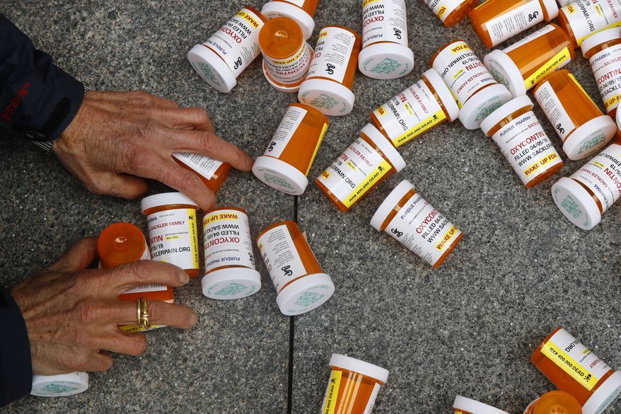 FILE - In this Friday, April 5, 2019, file photo, a protester gathers containers that look like OxyContin bottles at an anti-opioid demonstration in front of the U.S. Department of Health and Human Services headquarters in Washington, D.C. The U.S. has backed away from recommending opioids for long-term treatment of chronic pain. Nevertheless, companies continue pushing the drugs in other countries, and consumption is growing. Researchers in Brazil report, for example, that prescription opioid sales have increased 465 percent in six years. (AP Photo/Patrick Semansky)