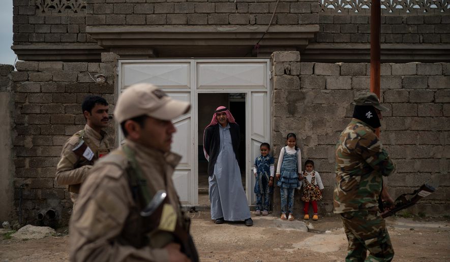 In this April 5, 2019, photo, residents watch as local militia and Iraqi army soldiers walk past their home during a raid in Badoush, Iraq. (AP Photo/Felipe Dana) ** FILE **