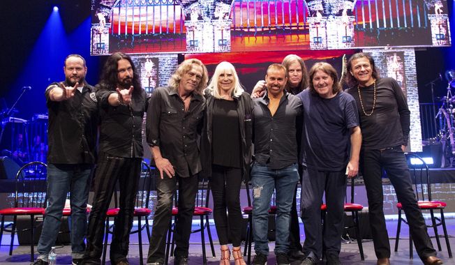 This May 23, 2019 photo released by Niji Entertainment shows, from left, singer Tim Owens, bassist Bjorn Englen, keyboardist Scott Warren, Wendy Dio, widow of Ronnie James Dio, Eyellusion CEO Jeff Pezzutti, guitarist Craig Goldy, drummer Simon Wright, singer Oni Logan posing to promote the Dio Returns tour. A hologram of Ronnie James Dio, who died nine years ago, will appear with a live band for the tour, which starts Friday in Ft. Myers, Fla. (Stephanie Cabral/Niji Entertainment via AP)