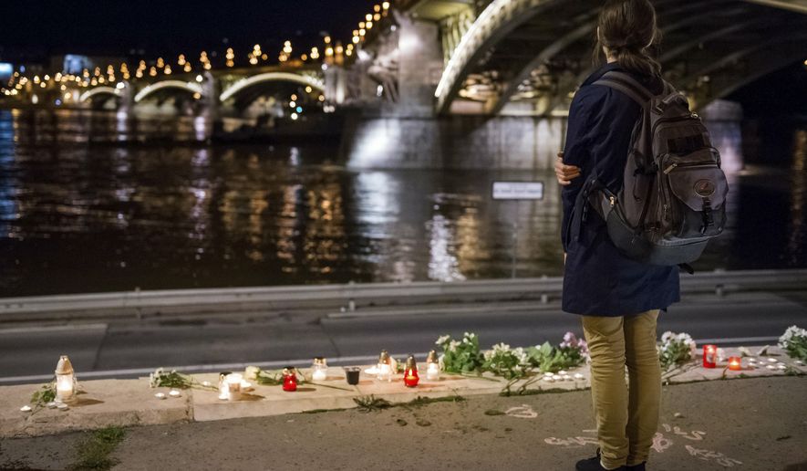 A woman stands by flowers and candles placed on the riverbank to pay tribute to the victims of the capsized boat at Margaret Bridge, in Budapest, Hungary, Thursday, May 30, 2019. Rescue crews in Hungary's capital are preparing to raise a sightseeing boat from the bottom of the Danube River Thursday as search teams scoured the waters for 21 people missing after the vessel, packed with South Korean tourists, collided with a larger cruise ship and sank. Seven people are confirmed dead and seven were rescued, all of them South Koreans. (Zoltan Mathe/MTI via AP)
