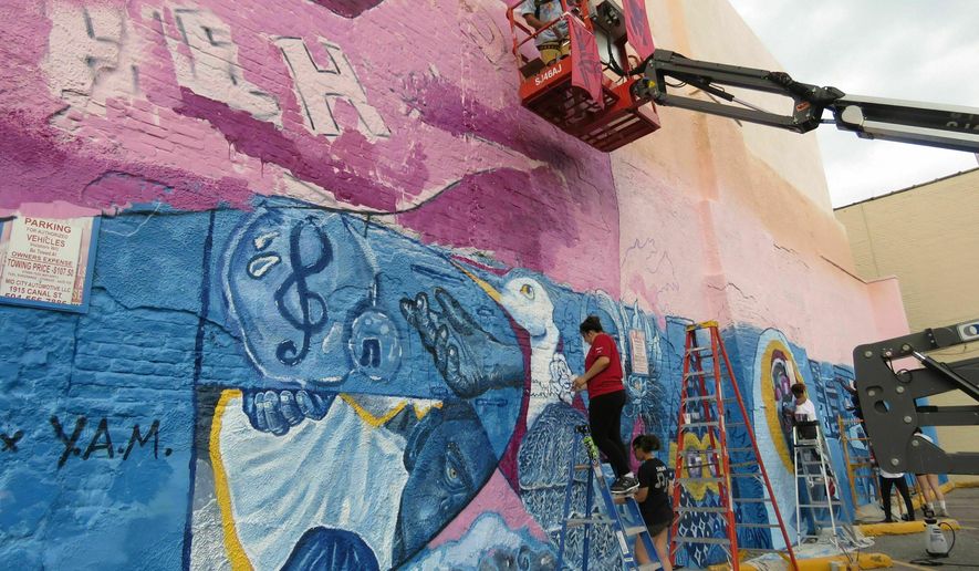 In this Thursday, May 30, 2019 photo, Brandon "BMike" Odoms, in man-lift, and students in the Young Artist Movement work on a mural in downtown New Orleans. The mural is one of five created as part of an Arts Council of New Orleans project called "Unframed." The council's executive director, Heidi Schmalbach, says the group wants New Orleans to be known for its contemporary art as much as for its music, food and culture. (AP Photo/Janet McConnaughey)