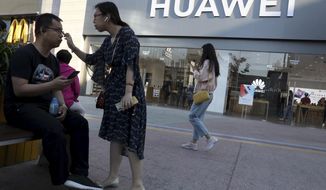 In this May 20, 2019, photo, a woman adjusts the glasses of a man outside a Huawei store in Beijing. The world&#39;s largest association of technology professionals has reversed a decision that would have excluded employees of Chinese tech giant Huawei and its affiliates from some editorial and peer review activities.(AP Photo/Ng Han Guan)