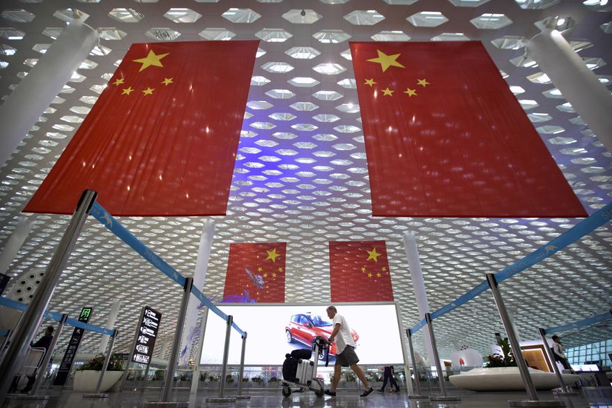 In this Oct. 10, 2018, file photo, a traveler pushes his luggage beneath large Chinese flags hanging from the ceiling in Shenzhen Bao'an International Airport in Shenzhen in southern China's Guangdong province. China has on Tuesday, June 4, 2019, issued a travel warning for the U.S., saying Chinese visitors have been interrogated, interviewed and subjected to other forms of what it called harassment by U.S. law enforcement agencies. (AP Photo/Mark Schiefelbein) **FILE**