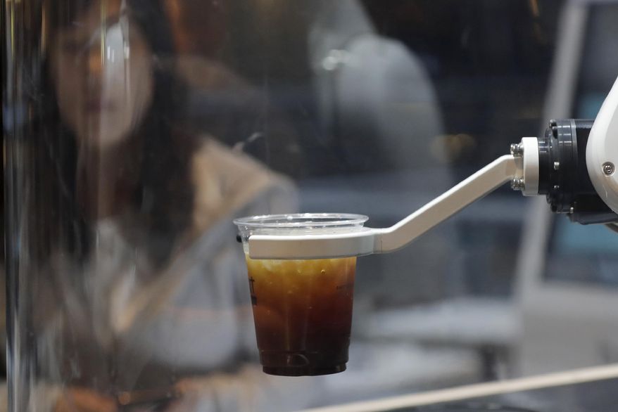 In this May 22, 2019, photo, a customer waits for a coffee in front of a robot after placing an order at a cafe in Seoul, South Korea. South Korea expands adoption of unmanned technology in businesses to meet the changing patterns of consumers who increasingly favor shopping or enjoying services with minimized human interactions and to reduce burdens of high labor costs. (AP Photo/Lee Jin-man)
