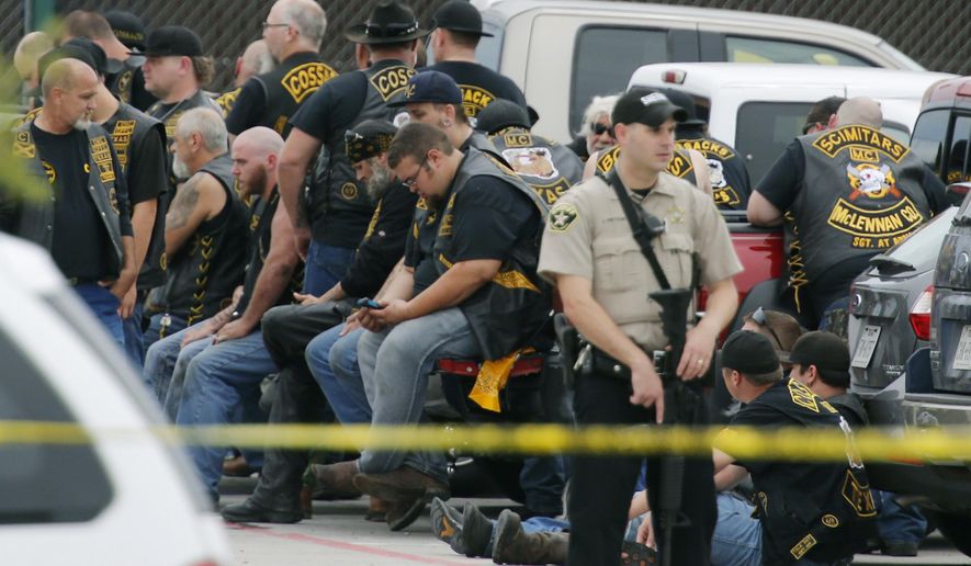 FILE - In this May 17, 2015 file photo, a McLennan County deputy stands guard near a group of bikers in the parking lot of the Twin Peaks restaurant in Waco, Texas. An attorney for six men arrested after the 2015 shootout between rival biker gangs that left nine people dead and at least 20 injured asked a district court judge Wednesday, June 5, 2019, to assign a special master to supervise the return of items seized from the nearly 200 detained bikers. (Rod Aydelotte/Waco Tribune-Herald via AP, File)