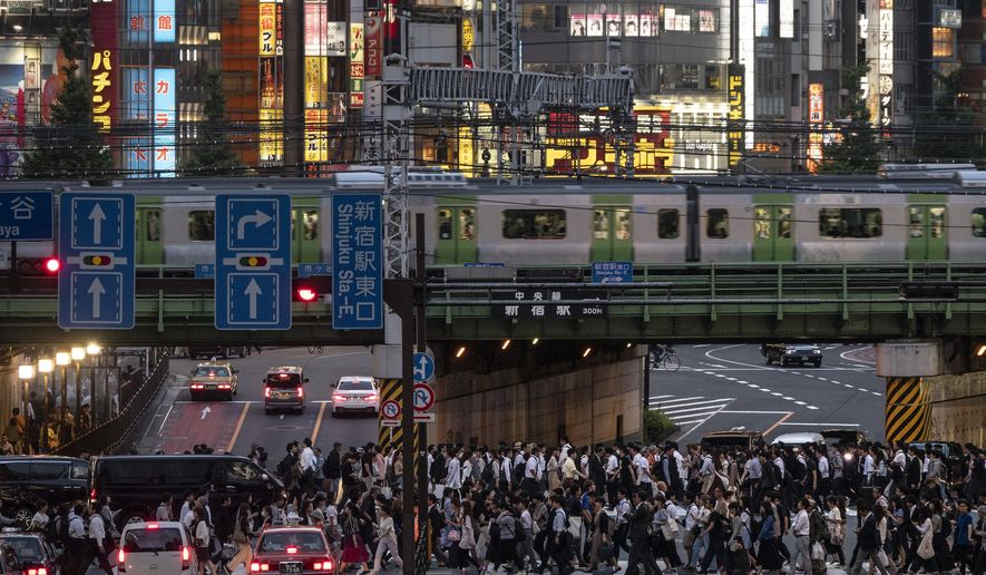In this Tuesday, June 4, 2019, photo, a Yamanote Line train travels above commuters walking across the crossing during evening rush hours in the Shinjuku district of Tokyo. Operated by the East Japan Railway Co., the Yamanote Line in Tokyo makes a loop around the center of the city, connecting 29 stations that include key stops such as Shinjuku, Shibuya and Ikebukuro. A complete loop of about an hour offers scenes of Japanese daily lives. (AP Photo/Jae C. Hong)