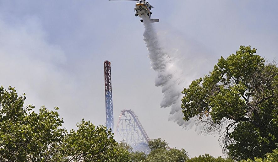 Los Angeles County Fire helicopter drops water on brush fire burning close to Six Flags Magic Mountain and Hurricane Harbor amusement park in Santa Clarita, Calif., Sunday, June 9, 2019. Heavy smoke surrounding Six Flags Magic Mountain and Hurricane Harbor prompted the park to announce an evacuation shortly after noon Sunday north of Los Angeles. But about 40 minutes later, the park said on its Twitter account that fire officials asked guests to stay at the park while they work to contain the blaze. Police closed access roads to the park off Interstate 5. (AP Photo/Rick McClure)