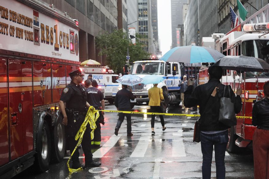 A policeman holds a tape to keep passersby away from the site of a helicopter crash, Monday, June 10, 2019 in New York. The New York City Fire Department says the pilot of a helicopter that crashed on a Manhattan skyscraper rooftop has died. (AP Photo/Mark Lennihan)