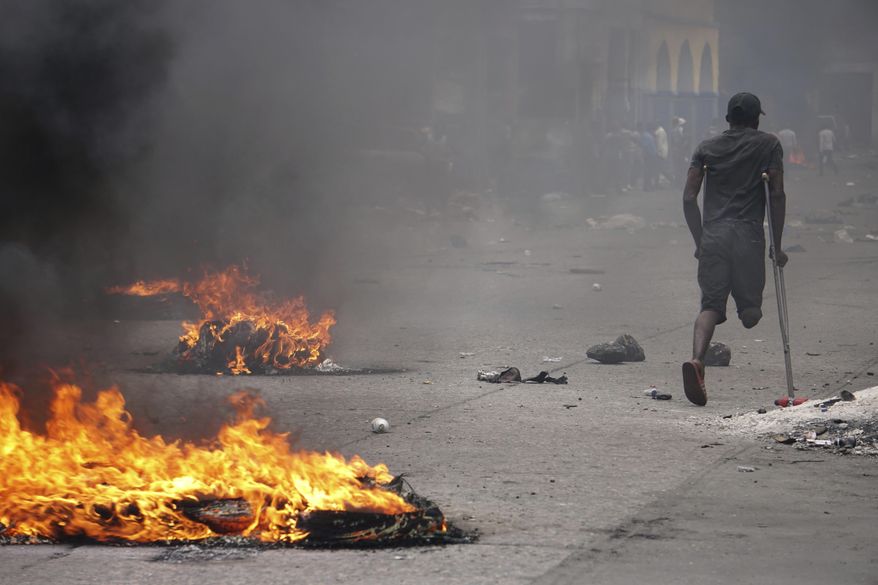 A protester on crutches passes burning tires during a demonstration to demand the resignation of President Jovenel Moise in Port-au-Prince, Haiti, Monday, June 10, 2019. Opposition leaders in Haiti launched a two-day strike that paralyzed the country's capital amid another day of protests demanding that President Jovenel Moise resign over corruption allegations. (AP Photo/Edris Fortune)