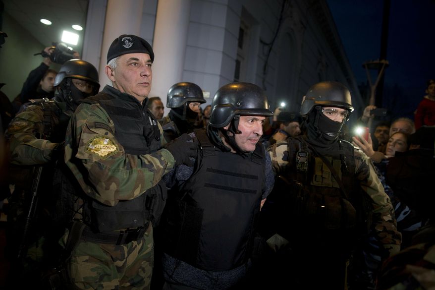 FILE - In this June 14, 2016 file photo, former Public Works Secretary Jose Lopez, center, is escort by police outside the a police station in the outskirts of Buenos Aires, Argentina. A court in Argentina sentenced Lopez on Wednesday, June 12, 2019, to 6 years in prison for illicit enrichment after he tried to hide millions of dollars in cash at a convent. (AP Photo/Natacha Pisarenko, File)