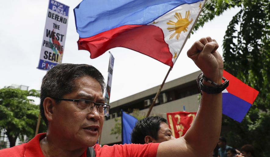 A protester raises his fist beside a national flag during a protest outside the Chinese Consulate in the financial district of Makati, metropolitan Manila, Philippines to mark Independence Day on Wednesday, June 12, 2019. The Philippine defense secretary says an anchored Filipino fishing boat has sunk in the disputed South China Sea after being hit by a suspected Chinese vessel which then abandoned the 22 Filipino crewmen. (AP Photo/Aaron Favila)