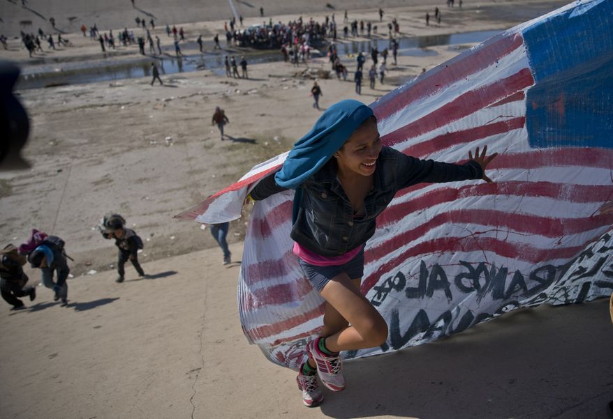 In this Nov. 25, 2018, file photo, a migrant woman helps carry a handmade U.S. flag up the riverbank at the Mexico-U.S. border after getting past Mexican police at the Chaparral border crossing in Tijuana, Mexico, as a group of migrants tries to reach the U.S. (AP Photo/Ramon Espinosa, File)