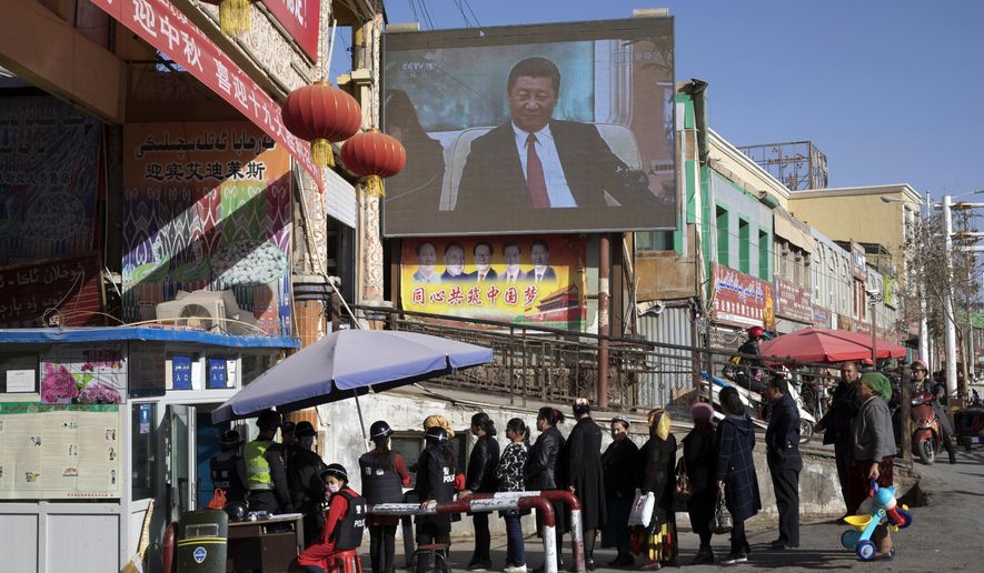 FILE - In this Nov. 3, 2017, file photo, residents walk through a security checkpoint into the Hotan Bazaar where a screen shows Chinese President Xi Jinping in Hotan in western China&#x27;s Xinjiang region. China says the U.N.&#x27;s counterterrorism chief visited Xinjiang last week despite protests from the U.S. and a rights group that the trip would be inappropriate in light of the human rights conditions in the far west region. (AP Photo/Ng Han Guan, File)