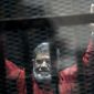 FILE - In this June 21, 2015 file photo, former Egyptian President Mohammed Morsi, wearing a red jumpsuit that designates he has been sentenced to death, raises his hands inside a defendants cage in a makeshift courtroom at the national police academy, in an eastern suburb of Cairo, Egypt. On Monday, June 17, 2019, Egypt&#39;s state TV said that the country&#39;s ousted President Mohammed Morsi has collapsed during a court session and died. (AP Photo/Ahmed Omar, File)
