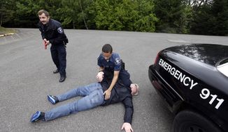 In this photo taken May 6, 2015, Seattle police recruits Travis Duennes, left, and Tre Smith work together through a practice scenario at the Washington State Criminal Justice Training Commission in Burien, Wash.  While some critics say that good officers already consider themselves protectors and that police need the best equipment to defend themselves and the public, many law enforcement leaders see a need for a broader change in police training and culture.  (AP Photo/Elaine Thompson)