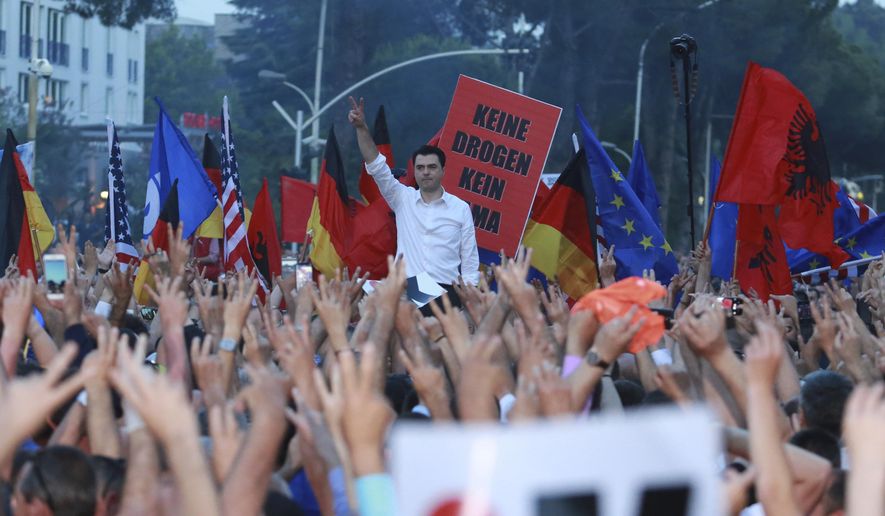 Lulzim Basha, leader of the main opposition Democratic Party, standing in background, flashes the victory sign during an anti-government protest in Tirana, Albania, Saturday, June 8, 2019. Thousands of Albanian opposition supporters are gathering in an anti-government protest while the United States and the European Union caution their leaders to disavow violence and sit in a dialogue to overcome the political crisis. The placard in background reads: “No drugs no”. (AP Photo/Hektor Pustina)