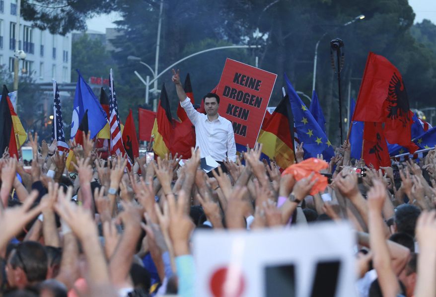 Lulzim Basha, leader of the main opposition Democratic Party, standing in background, flashes the victory sign during an anti-government protest in Tirana, Albania, Saturday, June 8, 2019. Thousands of Albanian opposition supporters are gathering in an anti-government protest while the United States and the European Union caution their leaders to disavow violence and sit in a dialogue to overcome the political crisis. The placard in background reads: “No drugs no”. (AP Photo/Hektor Pustina)