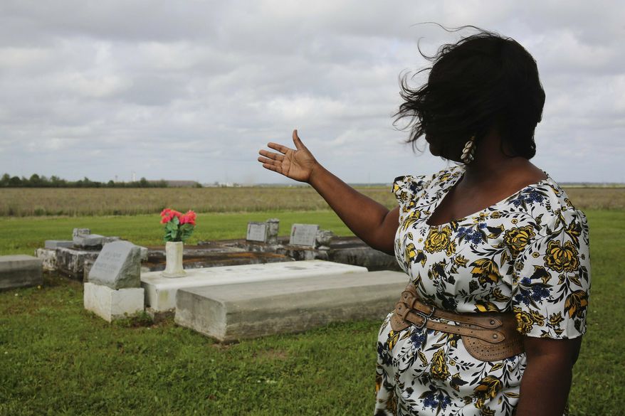 Slave descendant Carolyn Smith gestures towards gravestones of descendants of enslaved people, March 13, 2019, in Houma, LA. A new website that traces the family histories of hundreds of black slaves sold by Georgetown University and the Maryland Jesuits to southern Louisiana in 1838 has launched as the nation observes Juneteenth, the annual observance of the 1865 announcement of the abolition of slavery in America. The GU272 Memory Project website made public, Wednesday, June 19, 2019, includes documents, photographs and the indexed genealogies of thousands of descendants of the slaves, as well as recorded interviews with dozens of their living descendants. (Claire Vail/American Ancestors/New England Historic Genealogical Society via AP)