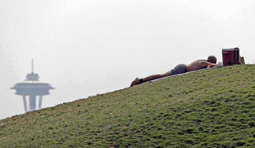 FILE - In this Aug. 9, 2017, file photo, a man sunbathes in view of the Space Needle, partially obscured by wildfire smoke covering the region from British Columbia fires, in Seattle. After subsequent years marked by thick smoke hanging over the city from summer wildfires, Seattle officials say they will retrofit five city facilities to serve as havens where residents can go to breathe clean air. (AP Photo/Elaine Thompson, File)