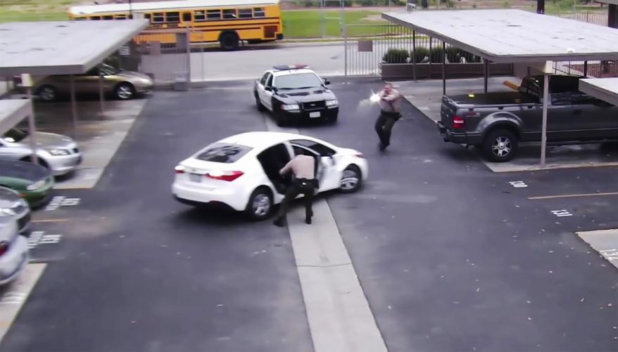 In this June 6, 2019 image from surveillance video provided by the Los Angeles County Sheriff's Department, a Los Angeles County sheriff deputy opens a rear door of a parked vehicle while a fellow office fires his gun at the car, fatally shooting Ryan Twyman. The video shows the reversing car's door striking the deputy before he and the other deputy open fire on the vehicle. The family of Twyman, who was unarmed during the incident, filed a claim for damages against Los Angeles County. (Los Angeles County Sheriff Department via AP)