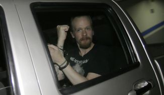 Swedish programmer Ola Bini gestures to the press in handcuffs as he is transferred away from the court where his Habeas Corpus request was accepted, before being freed on the condition that he appear periodically before a judge in Quito, Ecuador, Thursday, June 20, 2019. The Swedish programmer close to WikiLeaks founder Julian Assange has been held in jail for more than two months on suspicion of hacking. (AP Photo/Dolores Ochoa)