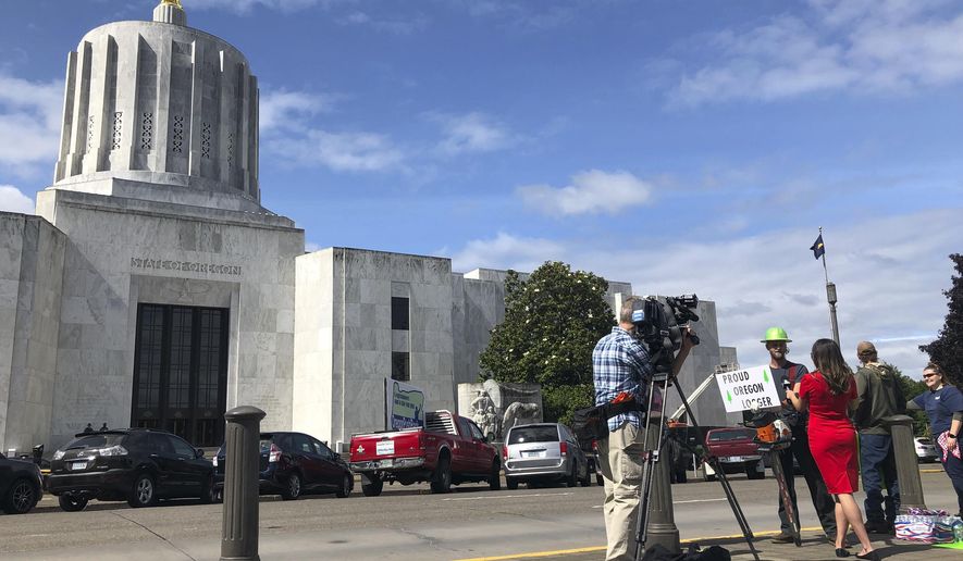 A TV reporter interviews self-employed logger Bridger Hasbrouck, of Dallas, Ore., outside the Oregon State House in Salem, Ore., on Thursday, June 20, 2019, the day the Senate is scheduled to take up a bill that would create the nation's second cap-and-trade program to curb carbon emissions. Senate Republicans, however, pledged to walk out so there wouldn't be enough lawmakers present for a vote on House Bill 2020, which is extremely unpopular among loggers, truckers and many rural voters. (AP Photo/Gillian Flaccus)