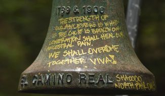 A detailed view of graffiti on an El Camino Real bell marker located at UC Santa Cruz is shown before being officially removed on Friday, June 21, 2019, in Santa Cruz, Calif. The cast-iron bell marker is one of hundreds in the state which memorializes the California Missions and viewed by the Amah Mutsun Tribal Band and other California indigenous people as a racist symbol that glorifies the domination of their ancestors. (AP Photo/Cody Glenn)