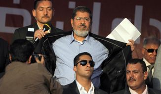 FILE - In this June 29, 2012 file photo, Egypt&#39;s President-elect Mohammed Morsi opens his suit jacket to show to his supporters that he is not wearing body armor at Tahrir Square, the focal point of Egyptian uprising, during his speech in Cairo, Egypt.  Morsi’s collapse and death in a Cairo courtroom on June 17, 2019,  was a brief rallying point for the Muslim Brotherhood whose influence waned dramatically in the Middle East since the 2013 military coup in Egypt which had widespread public support at the time. The long-running enmity between the Brotherhood and most Sunni-led governments highlights the deep divisions among Sunni Muslims. It adds a further complication to the volatile region, where the split between Sunnis and Shiite Muslims has created rival camps. (AP Photo/Amr Nabil, File)