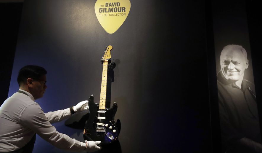 FILE - In this March 27, 2019, file photo, a technician arranges 'The Black Strat' from the collection of David Gilmour, guitarist, singer and songwriter of Pink Floyd, during a press opportunity at Christie's auction rooms in London. Christie’s auction house says it raised $21.5 million Thursday, June 20, 2019, selling off more than 120 guitars owned by the Pink Floyd guitarist, singer and songwriter. Proceeds went to ClientEarth, a non-profit fighting climate change. A black Stratocaster, dubbed the “Black Strat”, was the top item and was snatched up for $3,975,000, a new world record for a guitar at auction. (AP Photo/Kirsty Wigglesworth, File)