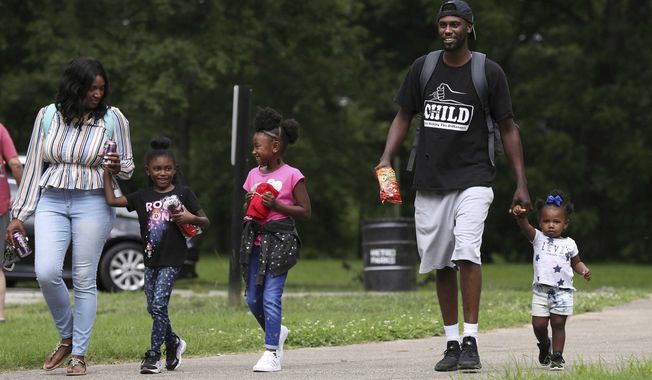 This photo taken June 12, 2019, shows Detrick Ellery walking with his daughter Derian Ellery, 1, right, while his other daughters Demi Ellery, 6, center, and Demiah Ellery, 6, joined them on their way to the playground at Shawnee Park in Louisville, Ky. Demiah and Derian&#x27;s mom Latasha Norfleet was at left. Detrick is enrolled in the 4 Your Child parenting skills program. (Sam Upshaw Jr./Courier Journal via AP)