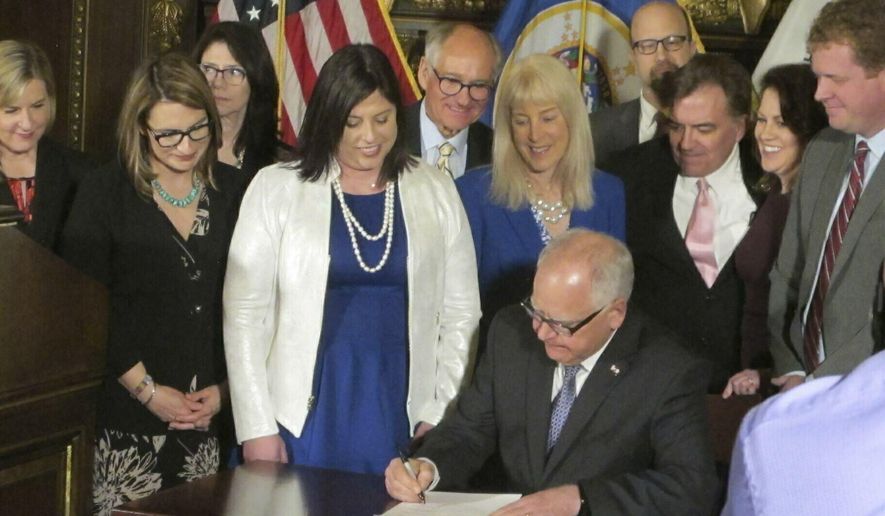 ADVANCE FOR MONDAY, JUNE 24 - FILE - In this May 2, 2019 file photo, Jenny Teeson, center in white, of Andover, Minn., looks on as Minnesota Gov. Tim Walz signs a bill at the State Capitol in St. Paul, repealing a Minnesota law that prevented prosecutors from filing sexual assault charges against people accused of raping their spouse. Teeson testified before legislative committees earlier this year about how her now ex-husband drugged her and made a video of himself raping her while she was unconscious. Starting July 1, Minnesotans who rape their spouses can be charged with sexual assault, wage theft will become a crime. (AP Photo/Steve Karnowski,File)
