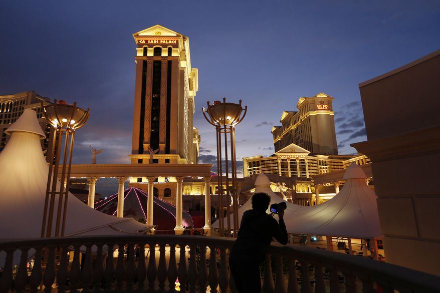 FILE - In this Jan. 12, 2015, file photo, a man takes pictures of Caesars Palace hotel and casino, in Las Vegas. Eldorado Resorts will buy Caesars in a cash-and-stock deal valued at $17.3 billion, creating a casino giant. The acquisition Monday, June 24, 2019, puts about 60 casinos and resorts in 16 states under a single name, one of the biggest gambling and entertainment ventures in the United States. (AP Photo/John Locher, File)