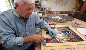 In this June 13, 2019 photo, Thom Berg demonstrates how he joins together the various pieces of stained glass by using lead came and a soldering iron as he works in his Northern Lights Design Studio in Aberdeen, South Dakota. (John Davis/Aberdeen American News via AP) **NOT AN AP PHOTO MEMBER**