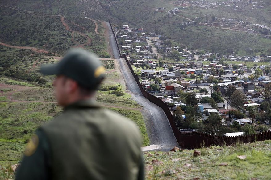 In this Feb. 5, 2019, file photo, Border Patrol agent Vincent Pirro looks on near a border wall that separates the cities of Tijuana, Mexico, and San Diego, in San Diego. Hundreds of thousands of people have been arriving at the border in recent months, many of them families fleeing violence and poverty in Central America. Once they reach the border, they can take different paths to try to get into the U.S. (AP Photo/Gregory Bull, File)
