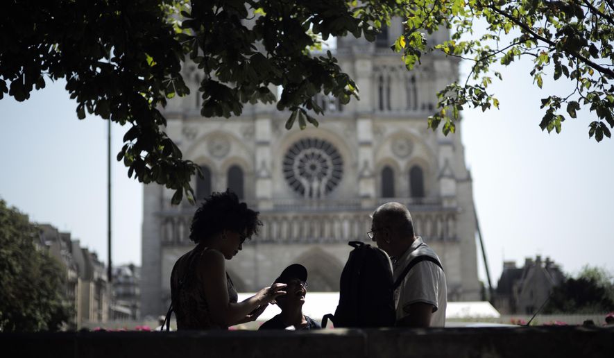 Tourists chat under a tree in front of Notre Dame Cathedral, Wednesday, June 26, 2019 in Paris. High temperatures are expected to go up to 39 degrees Celsius (102 Fahrenheit) in the Paris area later this week and bake much of the country, from the Pyrenees in the southwest to the German border in the northeast. (AP Photo/Kamil Zihnioglu)