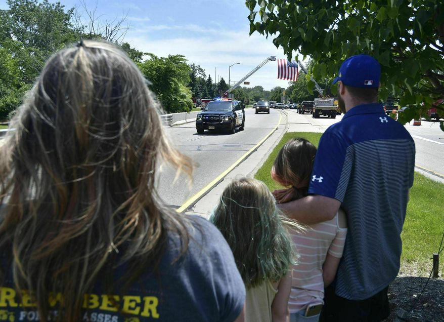 From right, Kyle Snyder, his daughters Alyssa, 10, and Ava, 12, and his mother, Lisa Meyers stand in the median of Sheridan Road to pay their respects as the procession for Racine police John Hetland makes its way down the road after his funeral at Carthage College in Kenosha, Wis., on Wednesday, June 26, 2019. (Sean Krajacic/The Kenosha News via AP)