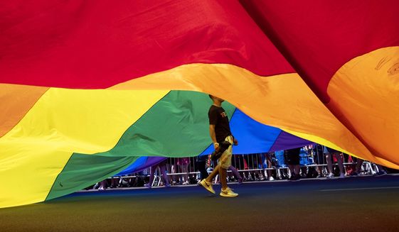 A participant walks under a large rainbow flag during the LBGTQ Pride march Sunday, June 30, 2019, in New York. (AP Photo/Craig Ruttle)