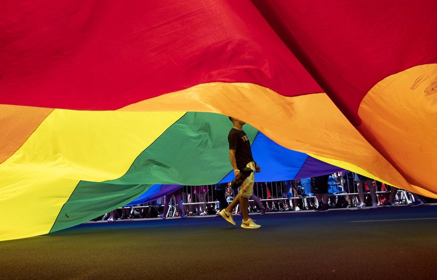 A participant walks under a large rainbow flag during the LBGTQ Pride march Sunday, June 30, 2019, in New York. (AP Photo/Craig Ruttle)