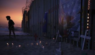 A youth stands by the border fence that separates Mexico from the United States, where candles and crosses stand in memory of migrants who have died during their journey toward the U.S., in Tijuana, Mexico, late Saturday, June 29, 2019. On the border fence at right hangs a cartoon depiction of a news photograph of the bodies of Salvadoran migrant Óscar Alberto Martínez Ramírez and his daughter Valeria, photographed on the banks of the Rio Grande between Matamoros, Mexico, and Brownsville, Texas, after they drowned on Sunday, June 23. (AP Photo/Emilio Espejel)