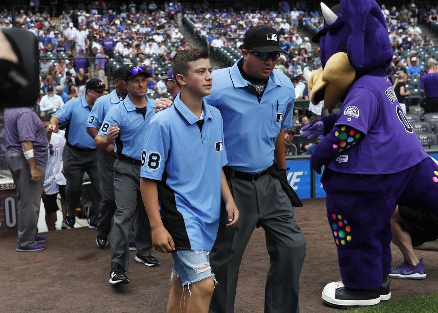 Thirteen-year-old Josh Cordova, left, of Denver, heads on the diamond with home plate umpire Cory Blaser before the Colorado Rockies host the Los Angeles Dodgers in the first inning of a baseball game Sunday, June 30, 2019, in Denver. The young man was officiating a youth baseball game when a brawl broke out among adults in the nearby suburb of Lakewood, Colo. (AP Photo/David Zalubowski) ** FILE **