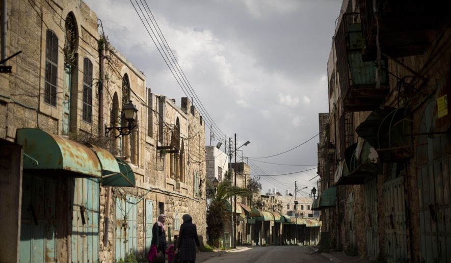 In this Wednesday, March 6, 2019, file photo, Palestinian women walk in a street where shops have been closed for a few years in the Israeli controlled part in the West Bank city of Hebron. The Falic family, owners of the ubiquitous chain of Duty Free America shops, fund a generous, and sometimes controversial, philanthropic empire in Israel that stretches deep into the West Bank. The family supports many mainstream causes as well as far right causes considered extreme even in Israel. (AP Photo/Ariel Schalit) ** FILE **