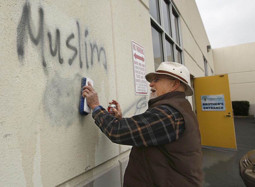 FILE - In this Feb. 1, 2017, file photo, Tom Garing cleans up racist graffiti painted on the side of a mosque in what officials called an apparent hate crime, in Roseville, Calif. California's attorney general says the number of reported hate crimes and victims decreased last year, although the number of suspects increased. The annual hate crime report released Tuesday, July 2, 2019, says hate crime events fell 2.5% from 2017. (AP Photo/Rich Pedroncelli, File)