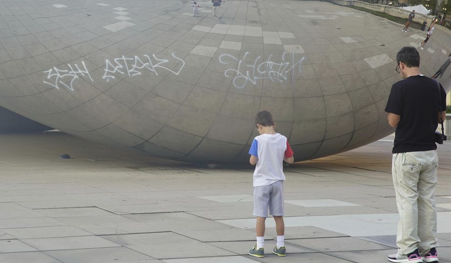Graffiti mars the popular giant metallic sculpture known as "The Bean," Tuesday, July 2, 2019, in Chicago. Police in Chicago have arrested seven people suspected of spray-painting graffiti on two downtown landmarks, including the popular giant metallic sculpture known as "The Bean." (Jermaine Nolen/Chicago Sun-Times via AP)