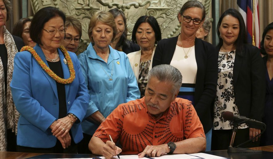 Hawaii Gov. David Ige, surrounded by members of the bipartisan Hawaii Women's Legislative Caucus and U.S. Sen. Mazie Hirono, at left wearing a lei, signs legislation in Honolulu, Tuesday, July 2, 2019, making Hawaii the first state in the U.S. to remove a requirement that a person be a victim of sex trafficking to have a prostitution conviction erased. (AP Photo/Audrey McAvoy)