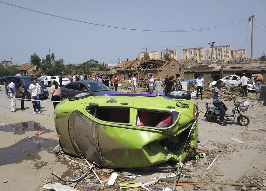 Residents past by an overturned car in the aftermath of a tornado in Kaiyuan in northeastern China's Liaoning province Thursday, July 4, 2019. A tornado blew through the city in northeast China, damaging factories and buildings, killing some people and injuring others, state media reported Thursday (Chinatopix Via AP)